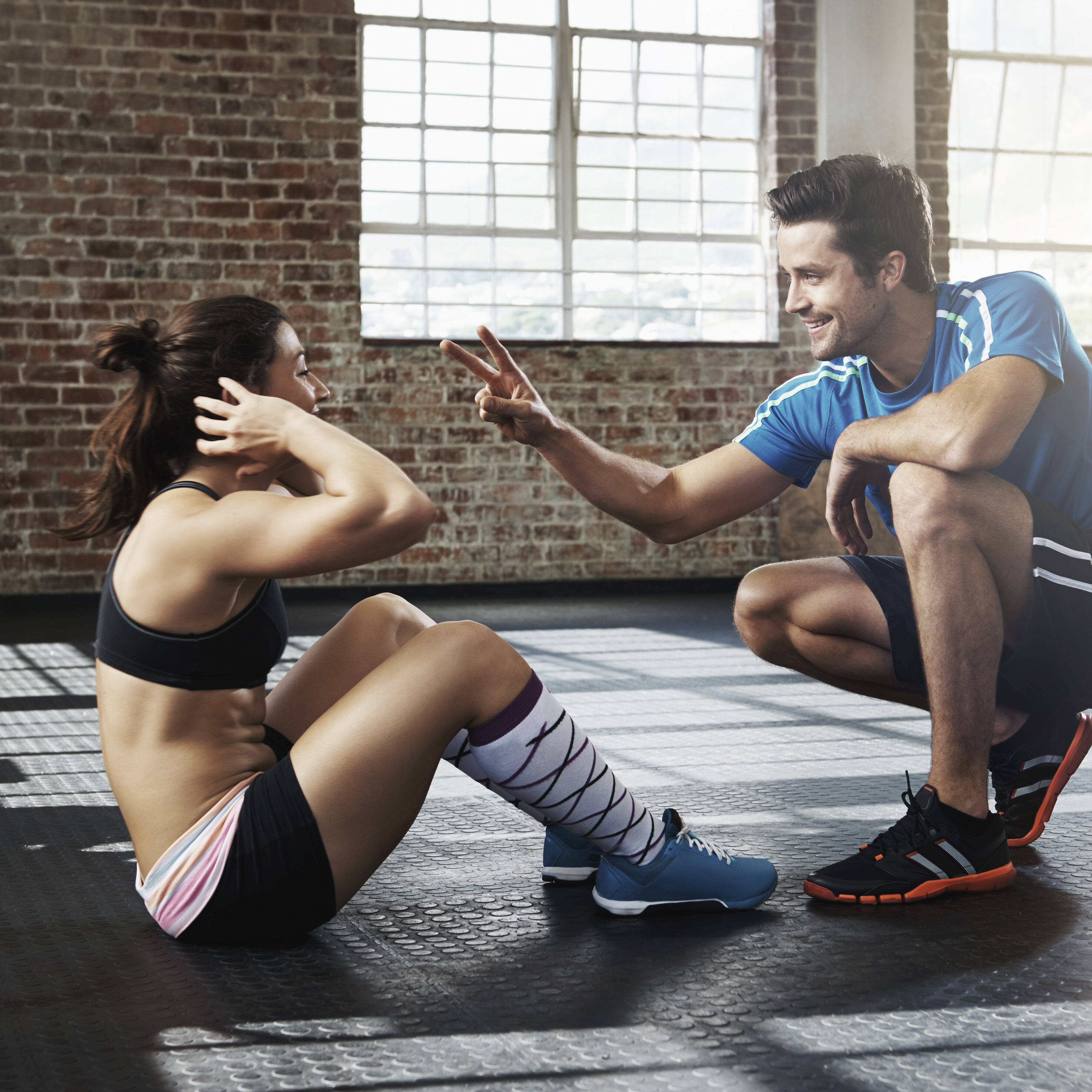 Cropped shot of young woman doing sit-ups while her trainer looks on